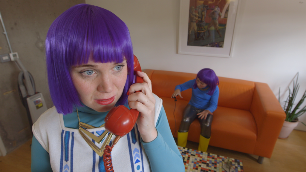 Still image from the film G_iRL. A women with purple hair talking on a red telephone. 