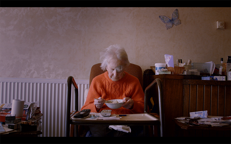 Still image from the Panorama Crisis in Care documentary. An old woman with an eye patch over one eye sitting in a chair in her living room eating from a bowl.