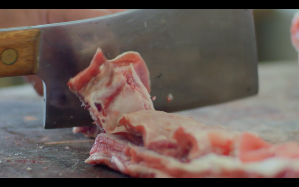 A close up photo of a butchers knife chopping meat