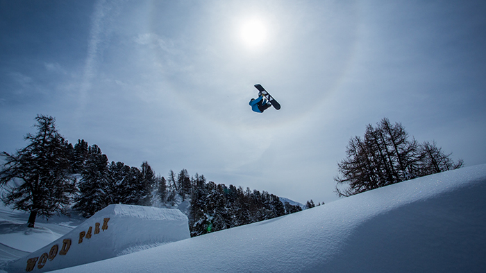 Jake Cornish doing a jump on his snowboard against the sun and blue sky